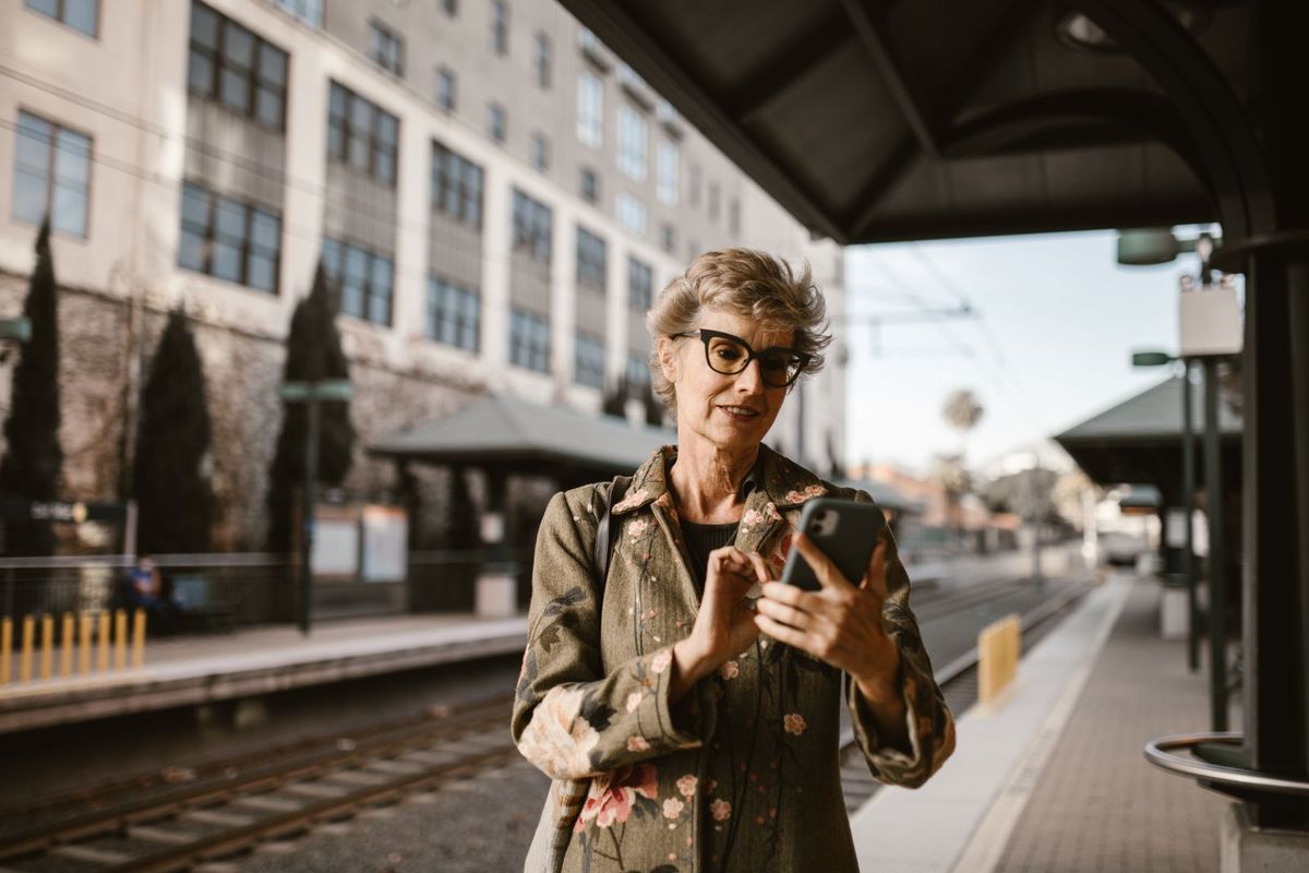 Frau um die 65 mit dem Smartphone am Bahnhof