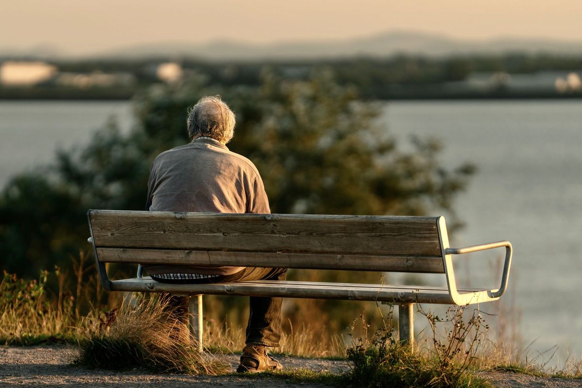 Mann sitzt am Abend allein auf einer Bank am See